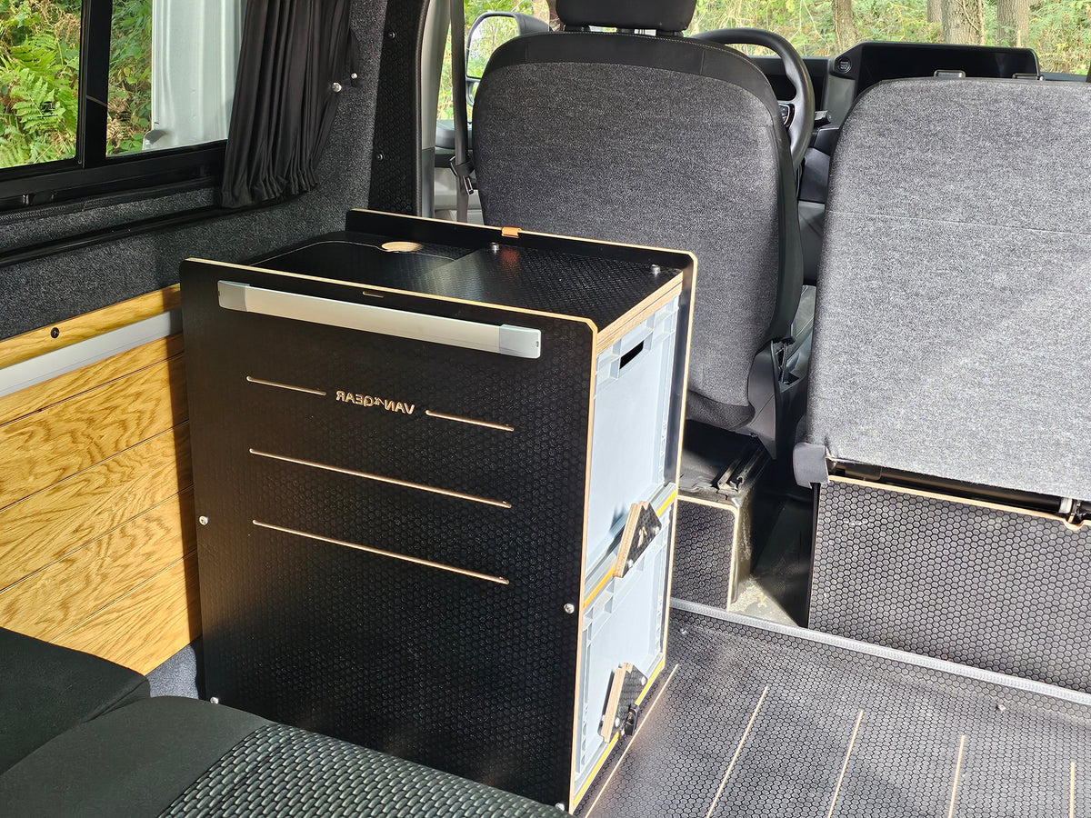 A black Van Gears portable refrigerator with a wood-grain trim handle, shown installed inside a vehicle's van conversion setup.