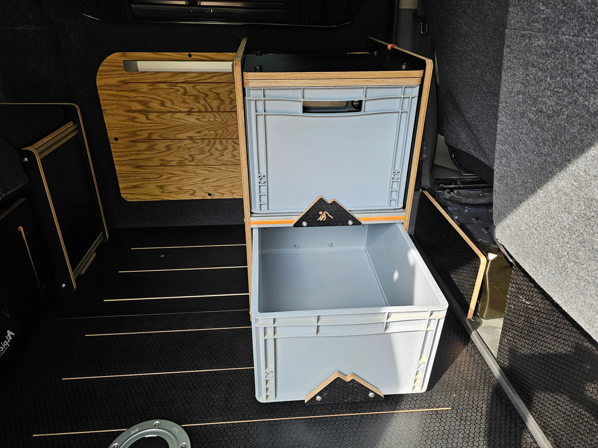 A set of light gray plastic storage bins with a natural wood frame, shown inside a vehicle or camper interior with a dark textured floor and wood paneling.